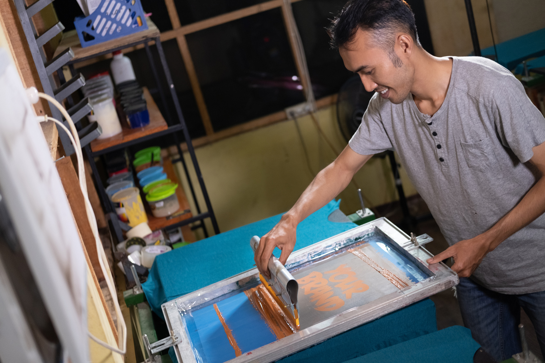 A Male Worker Uses a Screen Printing Squeegee to Print T-Shirts